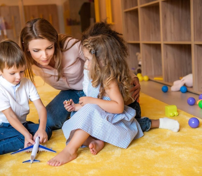 tutor-hugging-adorable-kids-on-carpet-in-kindergarten-1-pysk2n7n0bpk0ejlawo2ayffmiw89513pvyg3zuhjs